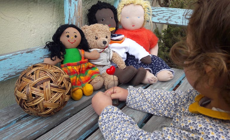 Puppen und Kuscheltiere sitzen auf einer Bank